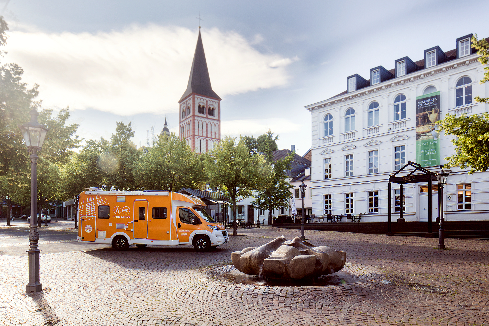 Das orangene rhenag Beratungsmobil steht auf dem Siegburger Marktplatz vor dem Museum.